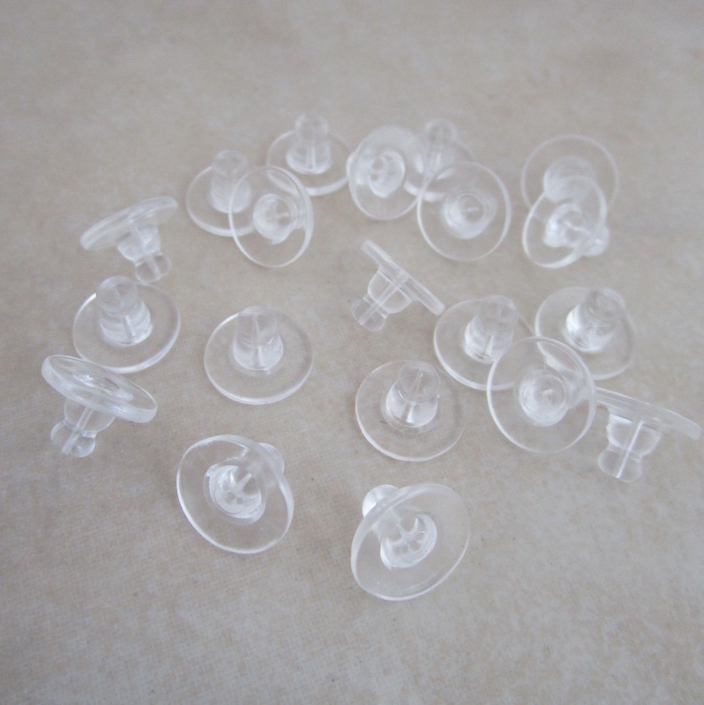 May include: A close-up of a group of clear plastic earring backs. The backs are designed to be used with post earrings.