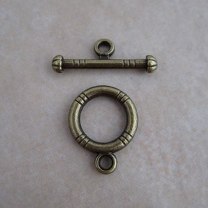 May include: Antique brass toggle clasp with a round ring and a decorative bar. The clasp is perfect for necklaces, bracelets, and other jewelry projects.