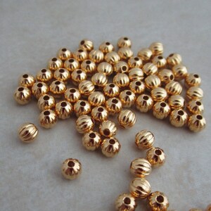 May include: A large pile of gold-colored metal beads with a ridged surface. The beads are round and have a shiny finish.