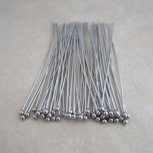 May include: A bundle of silver-toned head pins with round heads. The pins are arranged in a fan shape.
