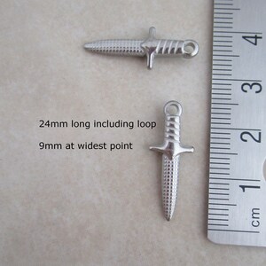 Op de afbeelding: Twee zilveren dolkbedels met een getextureerd oppervlak. De bedels zijn 24 mm lang inclusief de lus en 9 mm op het breedste punt.