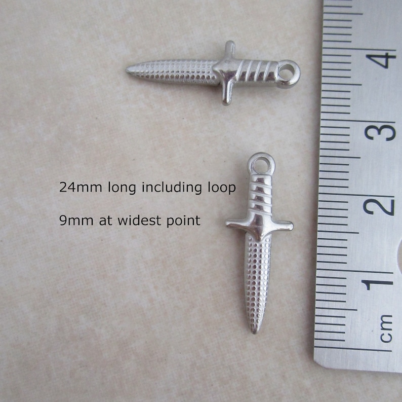 Op de afbeelding: Twee zilveren dolkbedels met een getextureerd oppervlak. De bedels zijn 24 mm lang inclusief de lus en 9 mm op het breedste punt.