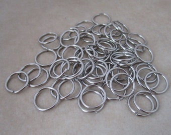 May include: A large pile of silver-toned metal key rings. The rings are all the same size and shape, and they are arranged in a random pattern.
