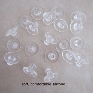 May include: A close-up of a group of clear silicone earring backs. The backs are soft and comfortable to wear.