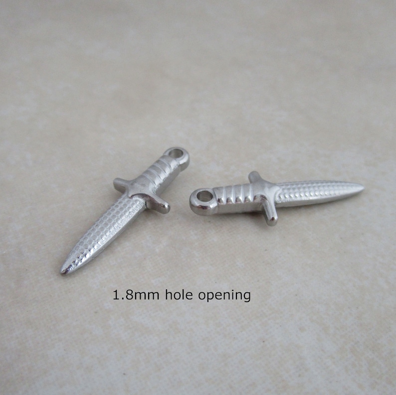 Op de afbeelding: Twee zilveren dolkbedels met een getextureerd oppervlak. Elke bedel heeft een opening van 1,8 mm.