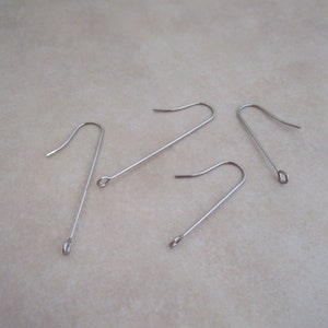 May include: Four silver earring hooks with a small loop at the top. The hooks are made of metal and are designed for attaching earrings.