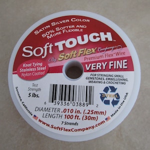 May include: A spool of Soft Touch Soft Flex Premium Flex Wire in silver color. The wire is very fine and has a test strength of 5 lbs. The spool is labeled with the brand name, product details, and a barcode. The wire is made in the USA.