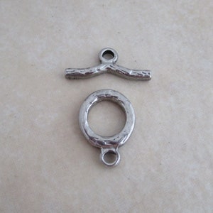May include: Two silver metal jewelry findings. One is a curved bar with a loop at the top. The other is a round ring with a loop at the bottom.