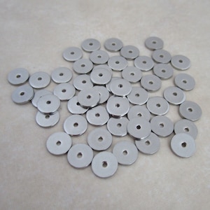 May include: A pile of silver metal spacer beads. The beads are round with a hole in the center.