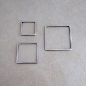 May include: Three silver metal square hoops of different sizes. The hoops are all made of the same material and have a smooth, polished finish.