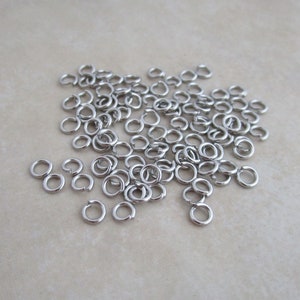 May include: A large pile of silver jump rings, a type of jewelry finding used for connecting chains, cords, and other jewelry components.