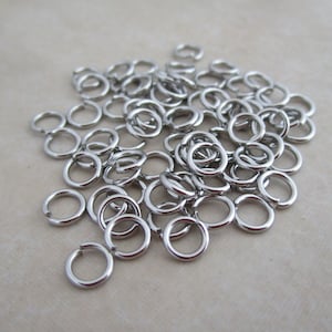 May include: A pile of silver jump rings, a type of jewelry finding used for connecting chains, cords, and other jewelry components.