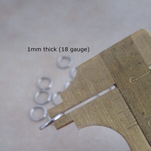 Puede incluir: Primer plano de un anillo de salto plateado que se mide con un calibre. El calibre indica 1 mm de grosor (18 galgas).