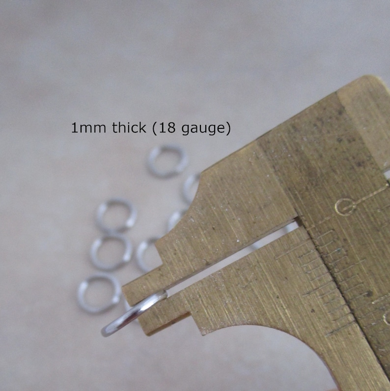 Puede incluir: Primer plano de un anillo de salto plateado que se mide con un calibre. El calibre indica 1 mm de grosor (18 galgas).