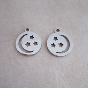 May include: Two silver metal charms in the shape of a circle with a crescent moon and four stars cut out.