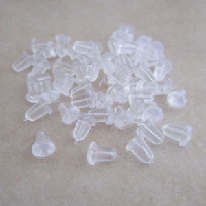 May include: A pile of clear plastic earring backs. The backs are small and have a rounded top and a pointed bottom.