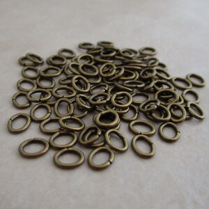 May include: A large pile of antique brass jump rings. The rings are oval shaped and have a smooth finish.