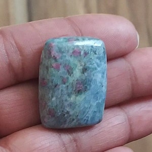 May include: A green and pink gemstone with a speckled pattern. The gemstone is rectangular and has a smooth, polished surface.