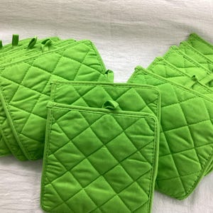 May include: A collection of bright lime green square pot holders featuring a diamond-shaped quilted pattern and a small fabric loop attached to the top corner of each piece for convenient hanging storage in a kitchen environment.
