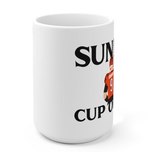 May include: White ceramic mug with black text that reads "Sunday Cup of Joe" and a cartoon image of a football player wearing an orange and black uniform.