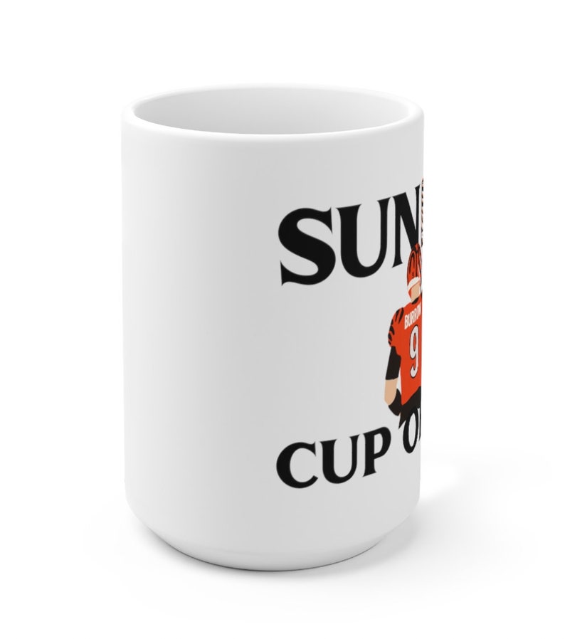 May include: White ceramic mug with black text that reads "Sunday Cup of Joe" and a cartoon image of a football player wearing an orange and black uniform.