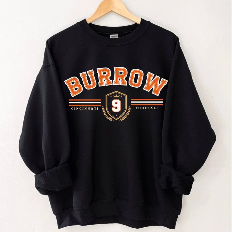 May include: Black sweatshirt with an orange and white graphic of the text "BURROW" in an arched design with a shield featuring the number "9" and the words "CINCINNATI FOOTBALL" underneath.