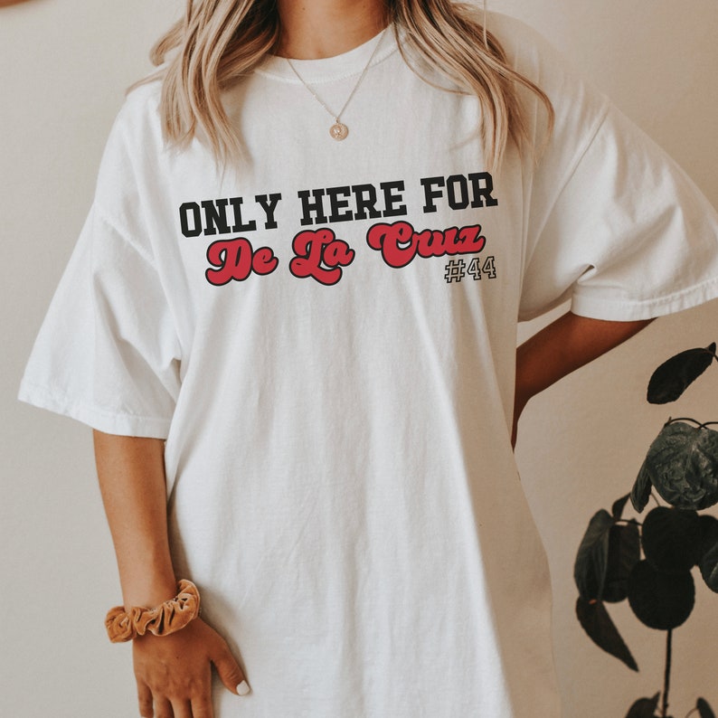May include: White t-shirt with black text that reads "ONLY HERE FOR De La Cruz #44". The text "De La Cruz" is in red.