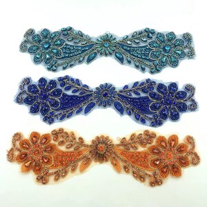 Puede incluir: Tres adornos de cuentas con forma de diseños florales. El primero es azul y turquesa, el segundo es azul y el tercero es naranja.