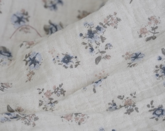 May include: Off-white fabric with a delicate floral pattern. The design features clusters of small flowers in shades of blue, pink, and gray, scattered across the surface. The fabric has a soft, textured appearance, suggesting a lightweight material.