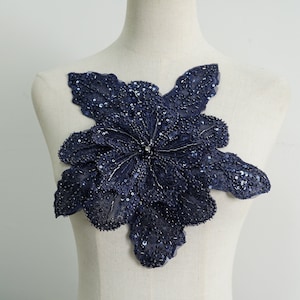 May include: A navy blue floral applique with sequins and beads. The applique is shaped like a flower with five petals.