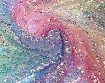 May include: A close-up of iridescent fabric with a swirling pattern of pink, blue, and white sequins. The fabric is soft and shimmery, and the sequins catch the light beautifully.