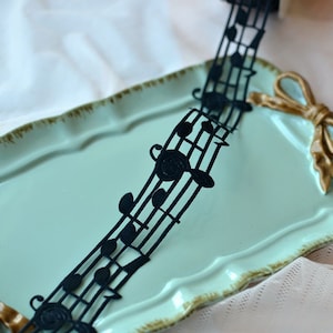 May include: Black ribbon with musical notes printed on it. The ribbon is on a light blue tray.