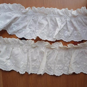 Puede incluir: Dos piezas de encaje de algodón blanco con borde festoneado y lazos bordados. El encaje tiene un aspecto fruncido y es perfecto para añadir un toque delicado a cualquier proyecto.