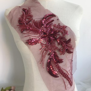 Op de afbeelding: Een bordeauxrode paillettenapplicatie met een bloemenmotief op een transparante mesh-stof. De applicatie is perfect om kleding, tassen of woonaccessoires een vleugje glamour te geven.