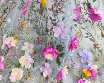 May include: A light blue fabric with an intricate floral design. The fabric features embroidered stems and leaves with colorful, three-dimensional flowers in shades of pink, yellow, and purple. The flowers are of varying sizes and add depth to the design.