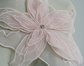 May include: A delicate pink flower applique with a beaded center and a single rhinestone. The applique is made of sheer fabric and has a delicate, feminine look.