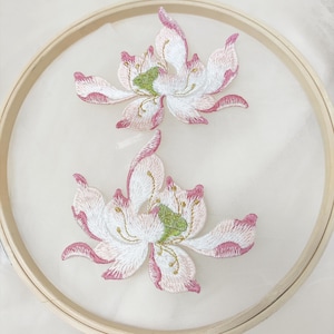 Op de afbeelding: Twee delicate geborduurde bloemenapplicaties in roze, wit en groene tinten. De bloemen hebben een delicaat, vrouwelijk ontwerp en zijn perfect om een ​​toets van elegantie aan elk project toe te voegen.