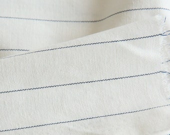 May include: White fabric with thin, dark blue stripes. The fabric is folded and has a slightly textured surface.