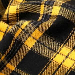 May include: Close-up of a yellow and black plaid fabric. The fabric is woven with a classic check pattern, featuring alternating squares of bright yellow and solid black. The texture appears soft and slightly textured, with visible threads.