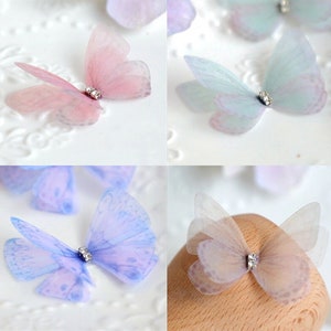 May include: Assortment of delicate butterfly embellishments with iridescent wings and clear rhinestone accents. The butterflies are in shades of pink, blue, and white.