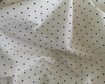 May include: White fabric with a black polka dot pattern. The fabric is folded and has a soft, textured appearance.