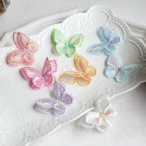 Può includere: Assortimento di otto applicazioni di farfalla colorate in tessuto trasparente. Le farfalle sono di vari colori pastello, tra cui rosa, blu, giallo e verde.