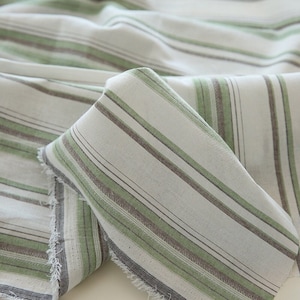 Könnte beinhalten: Weißer Stoff mit grünen und braunen Streifen. Der Stoff ist gefaltet und hat eine rohe Kante.