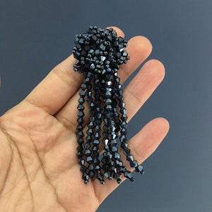 May include: Black crystal beaded tassel with a round, clustered top. The tassel is approximately 5 inches long.