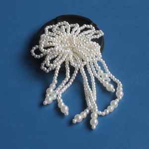 Puede incluir: Un broche de flor de perlas blancas con un racimo de perlas en el centro y largos hilos de perlas que cuelgan.