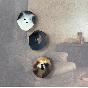 May include: Three round buttons with a mottled pattern. The buttons are black, white, and brown with two holes each.