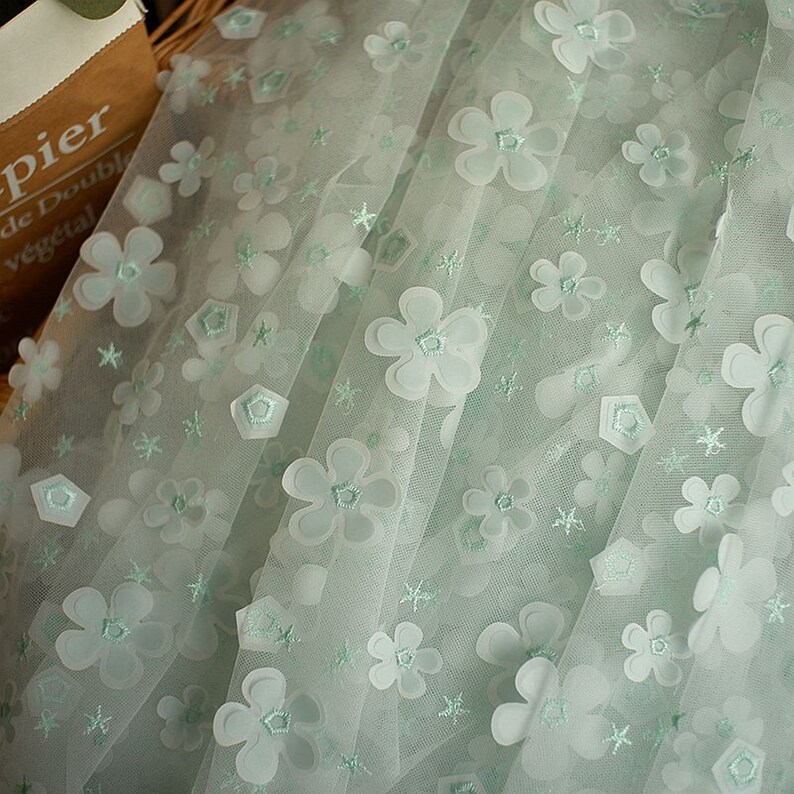 May include: Pale green tulle fabric with white 3D flower embellishments and smaller star-shaped embroidery.