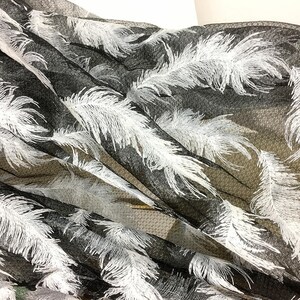 May include: Black sheer fabric with white embroidered feathers. The fabric is draped and folded, showing the texture of the mesh and the detail of the feathers.