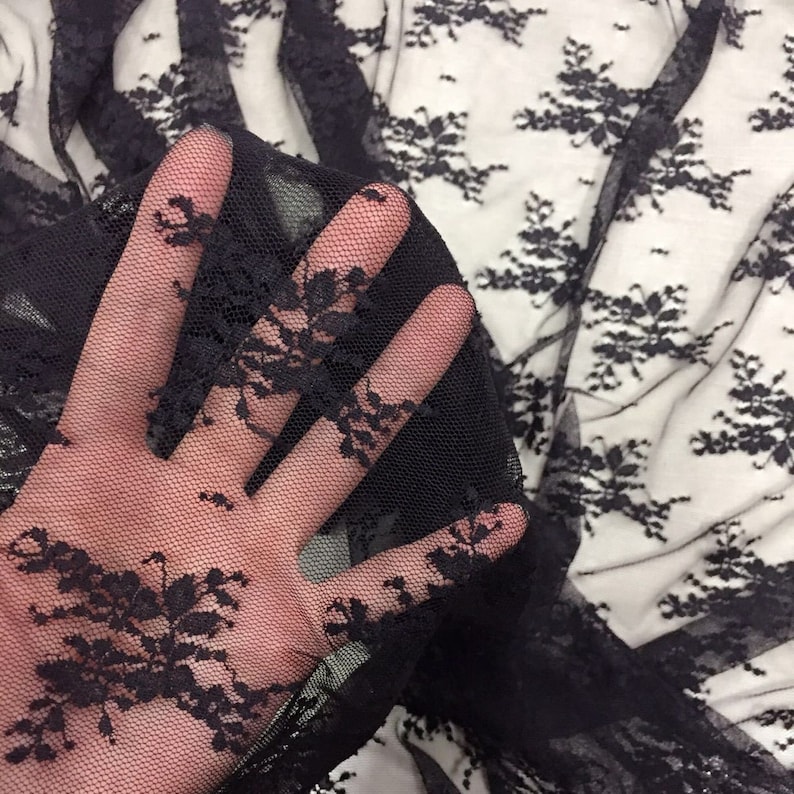May include: Black lace fabric with a delicate floral pattern. The fabric is sheer and has a soft, flowing texture.