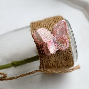 May include: A clear glass vase wrapped in brown twine with a pink and white butterfly embellishment.